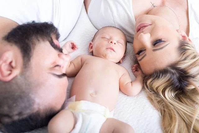 man, woman and baby asleep on a bed